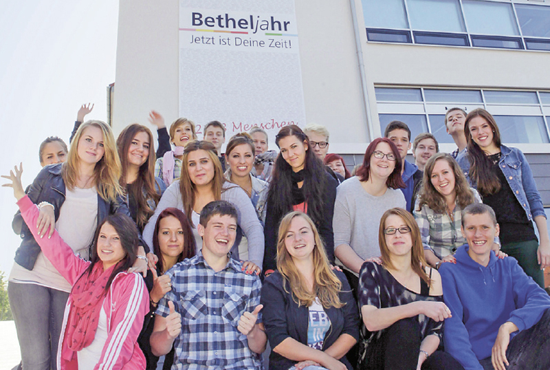 Eine groe Gruppe Betheljahr-Teilnehmender streckt den Daumen hoch vor einem Plakat fr das Betheljahr