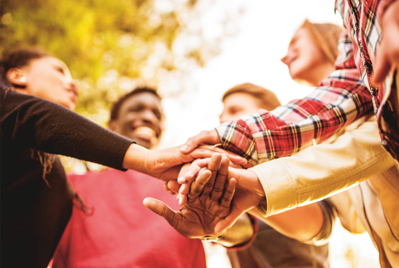 Symbolbild Teamarbeit: Eine Gruppe junge Leute im Kreis stehend macht einen Hnde-Stapel