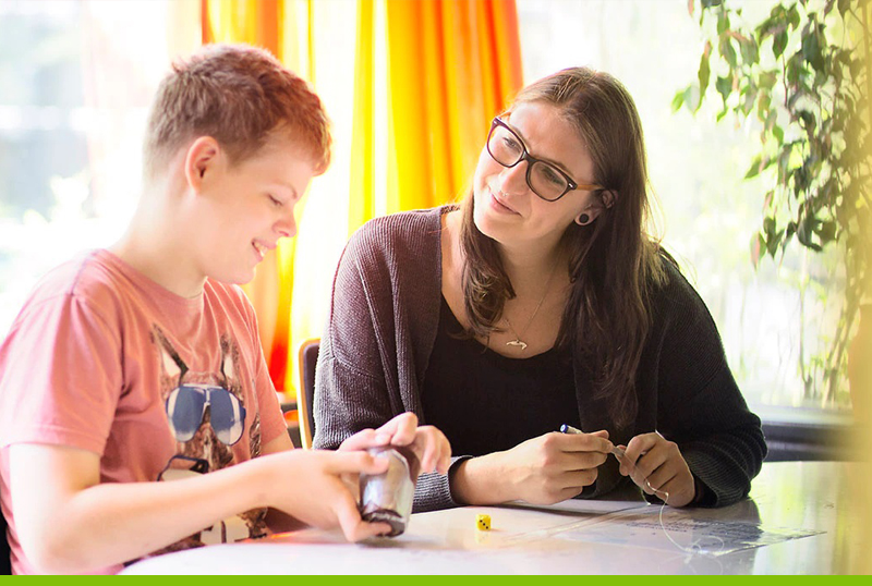 Eine junge Mitarbeiterin bgleitet einen Jugendlichen beim Wrfeln als Rechenaufgabe
