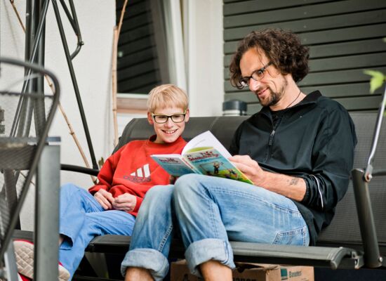 Ein Mitarbeiter liest einem Jugendlichen in einer Hollywood-Schaukel sitzend vor