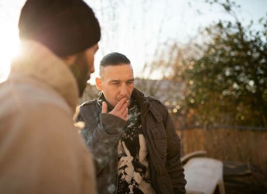 Ein rauchender Klient steht mit einem Begleiter im herbstlichen Garten