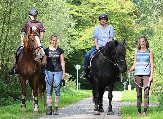 Zwei Klienten im Sattel auf Pferden des therapeutisches Reiten Bethel werden von zwei Mitarbeiterinnen ausgefhrt