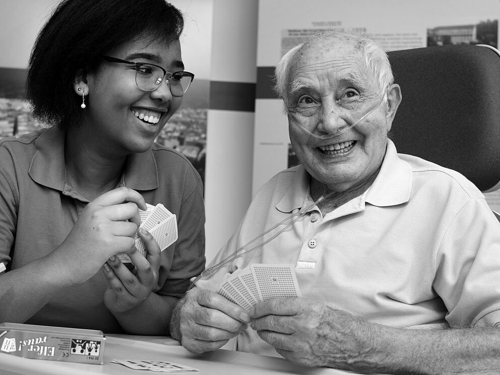 Eine junge Frau spielt mit einem lteren Mann im Krankenhaus Karten