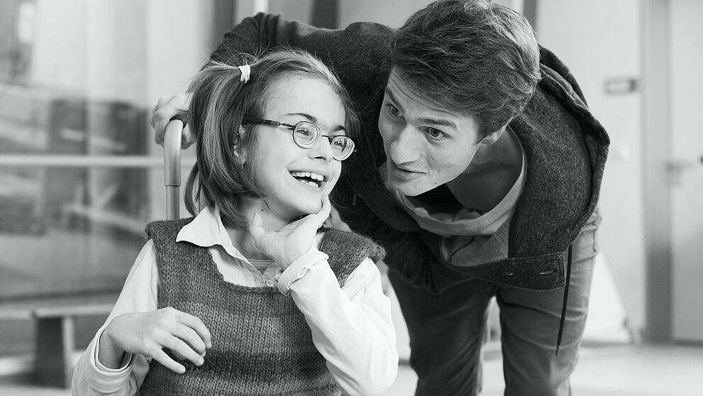 Ein junger Mann beugt sich im Gesprch zu einem Mdchen im Rollstuhl herunter